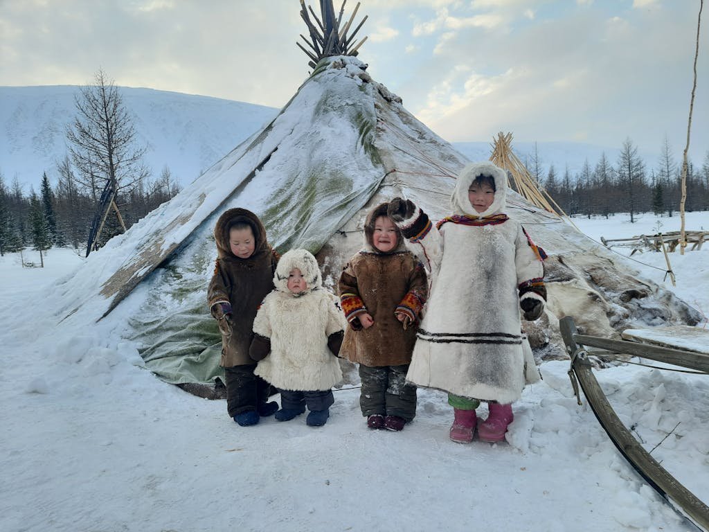 Children in traditional attire posing by a tent in a snowy winter landscape.