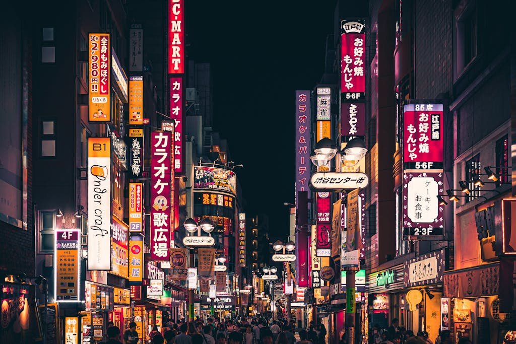 Night view of a busy Tokyo street with vibrant neon signs and people walking in Shinjuku, Japan.